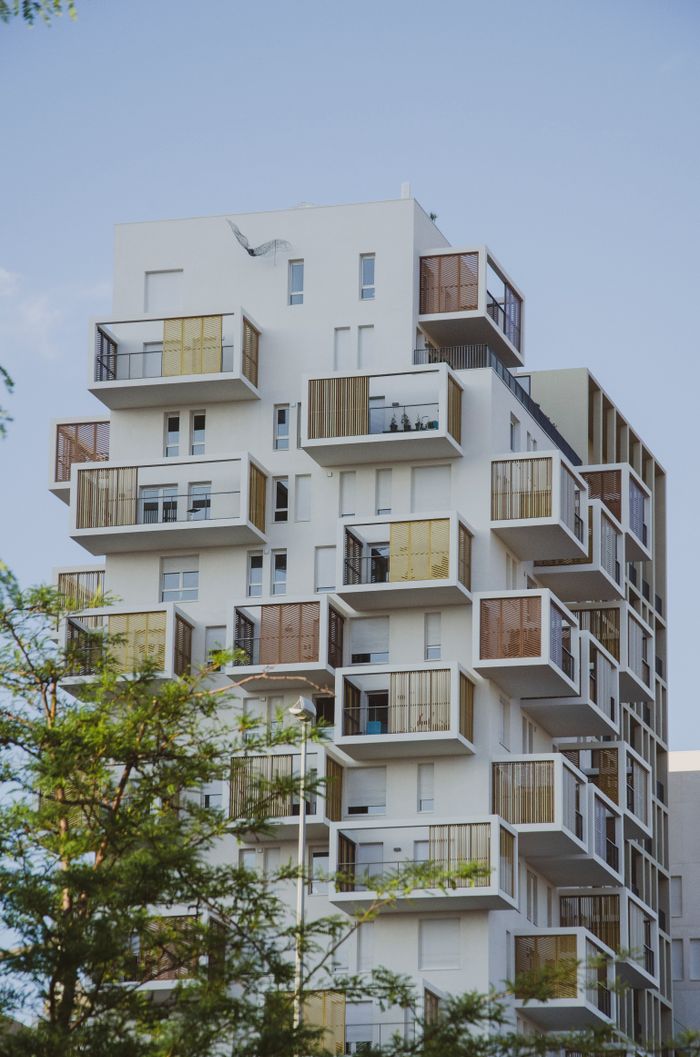 A contemporary apartment building with unique balcony design, set in an urban neighborhood.